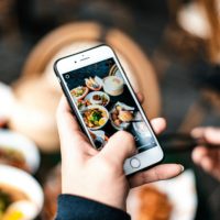 A person holding a mobile phone taking a picture of their food